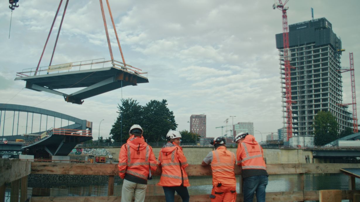 Brückensegment der Brücke Entenwerder hängt am Kran über dem Oberhafenkanal während Fachkräfte den Einhub beobachten