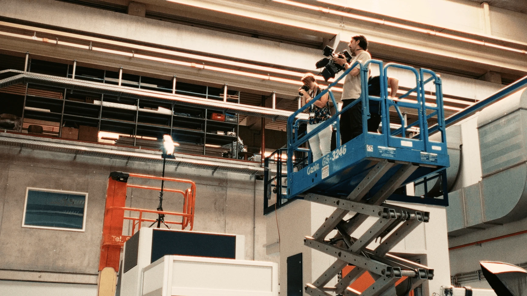 Filmteam von Lichtzug auf einer Arbeitsbühne bei einer Produktion in einer Industriehalle