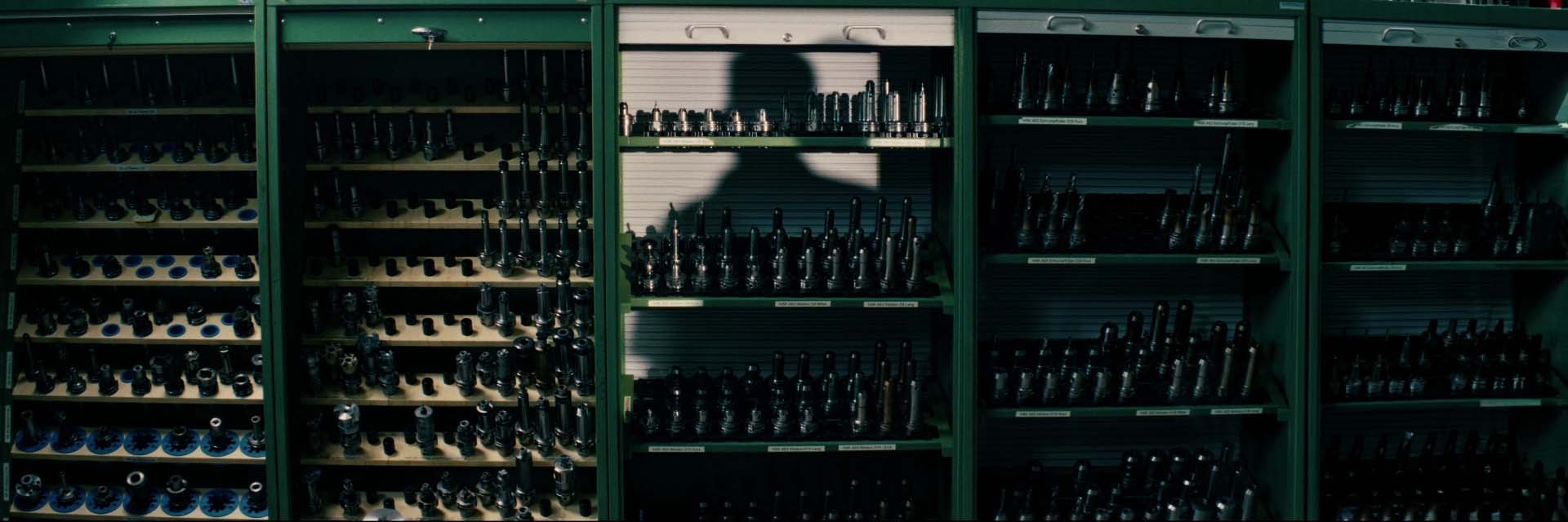 Werkzeugschränke in der Feinwerktechnik mit dem Schatten eines Mitarbeiters im Industriefilm für Behrens