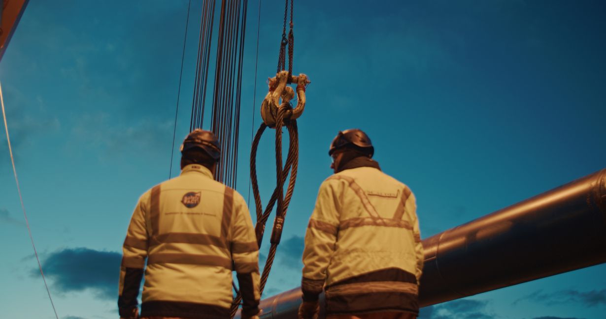 Zwei Offshore-Fachkräfte in Schutzkleidung prüfen Anschlagmittel an Deck