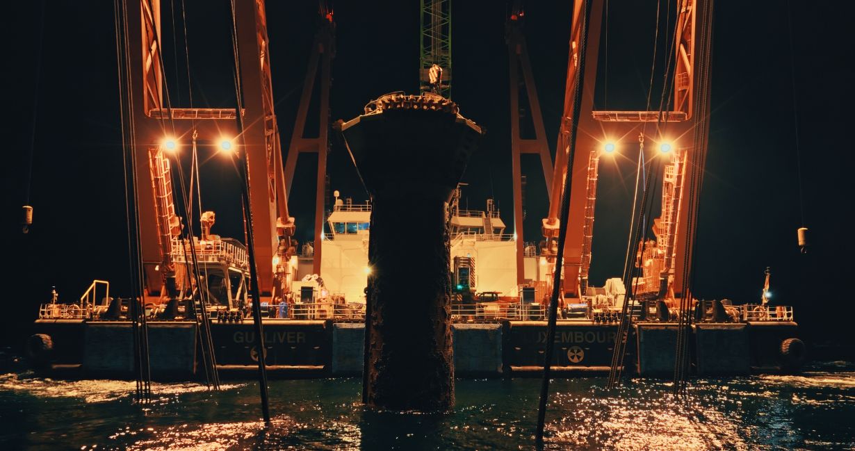Messmastfundament wird nachts zwischen den Kränen eines Arbeitsschiffs aus dem Wasser gehoben